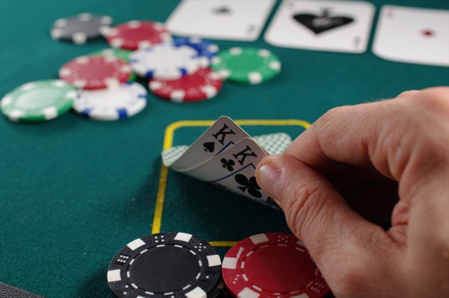 Hand eines Pokerspielers mit Karten und Chips.